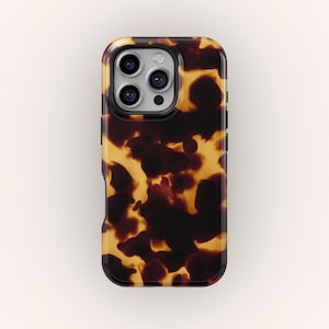 Puede incluir: Una funda de teléfono con un patrón de carey. La funda tiene un acabado brillante y una combinación de colores marrón oscuro y amarillo. La funda tiene un borde negro y recortes para la cámara y los botones del teléfono.
