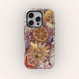 May include: A phone case with a beaded design featuring a sun, orange slice, and starfish. The case has a black border and a camera cutout. The design includes pink, gold, and purple beads, creating a textured surface.