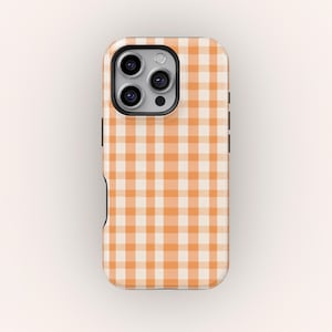 Puede incluir: Funda de teléfono con un patrón de cuadros vichy naranja y blanco. La funda tiene un borde negro y un recorte para la cámara. El diseño es un patrón de cuadros repetido, creando un aspecto simple pero elegante.