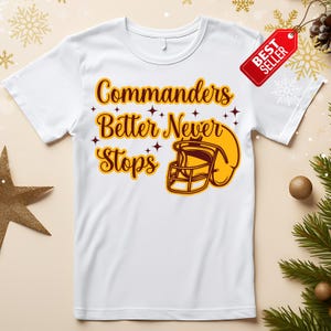 以下が含まれることがあります： 茶色と黄色の「Commanders Better Never Stops」の文字とフットボールのヘルメットのグラフィックが特徴の白いTシャツ。赤い「ベストセラー」タグがシャツに付いています。