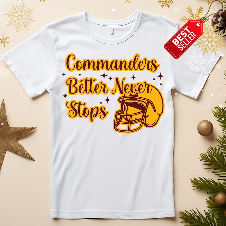 以下が含まれることがあります： 茶色と黄色の「Commanders Better Never Stops」の文字とフットボールのヘルメットのグラフィックが特徴の白いTシャツ。赤い「ベストセラー」タグがシャツに付いています。
