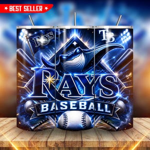 May include: A cylindrical tumbler featuring a Tampa Bay Rays baseball theme with a blue and white color palette. The design includes a stingray mascot, a baseball, bats, the text Rays Baseball, and the TB logo against a glowing stadium background.