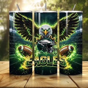 May include: A set of three stainless steel tumblers featuring a green and black design with an eagle, football helmet, and footballs. The word "EAGLES" is displayed in green and gold. The tumblers have a silver straw.