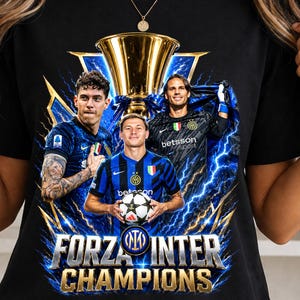 Pode incluir: Camiseta preta com um gráfico de três jogadores de futebol, um troféu dourado e raios. O texto "FORZA INTER CHAMPIONS" está em ouro e azul. Os jogadores usam camisas de futebol azuis e pretas.