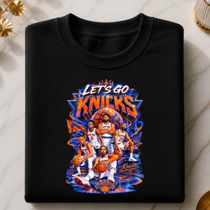 May include: Black sweatshirt featuring a graphic of the New York Knicks basketball team. The design includes the words "LET'S GO KNICKS" in blue and orange, along with illustrations of players and a basketball.