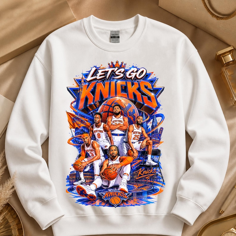 May include: White sweatshirt featuring a graphic of the New York Knicks basketball team. The design includes the words "Let's Go Knicks" in orange and blue, along with illustrations of players and a basketball court.