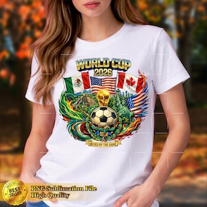 May include: White t-shirt featuring a colorful graphic for the 2026 World Cup. The design includes a soccer ball, flags of Mexico, the United States, and Canada, and the text "WORLD CUP 2026". The phrase "UNITED BY THE GAME" is also included.