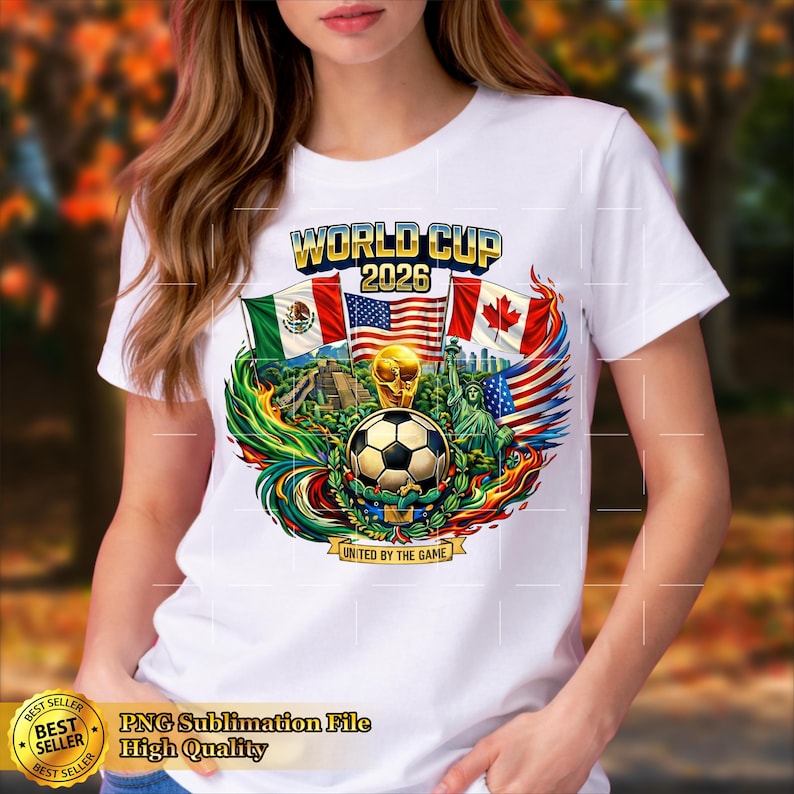 May include: White t-shirt featuring a colorful graphic for the 2026 World Cup. The design includes a soccer ball, flags of Mexico, the United States, and Canada, and the text "WORLD CUP 2026". The phrase "UNITED BY THE GAME" is also included.