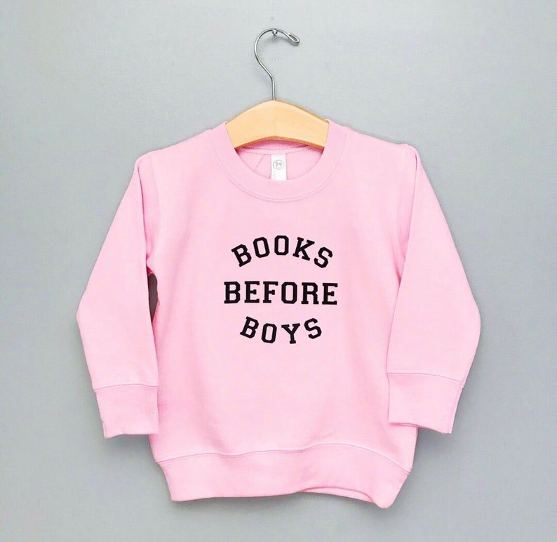 May include: Pink sweatshirt with black text that reads "BOOKS BEFORE BOYS".