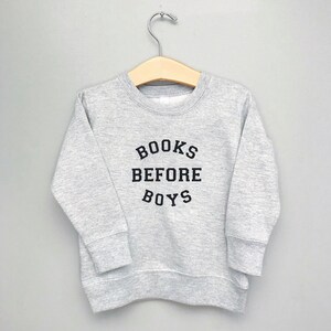 May include: A gray sweatshirt with the text "BOOKS BEFORE BOYS" printed in black.