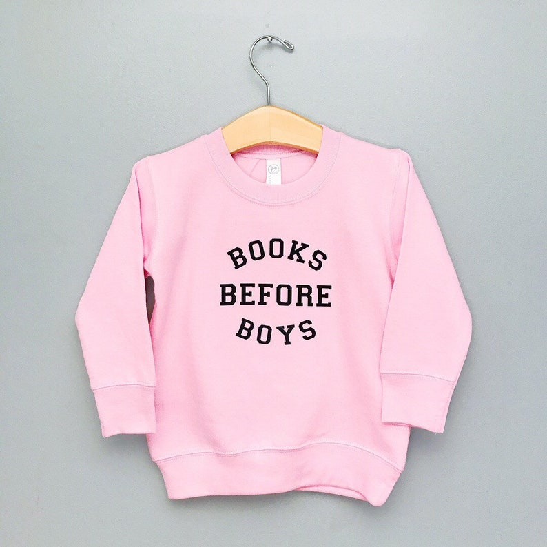 May include: Pink sweatshirt with black text that reads "BOOKS BEFORE BOYS".