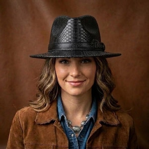 Op de afbeelding: Een zwarte fedora hoed met een gestructureerd slangenleerpatroon op de kroon en rand, voorzien van een bijpassende zwarte band rond de basis. De hoed toont de tekst Diamond Bits in een subtiel lettertype aan de zijkant van de kroon boven de band.
