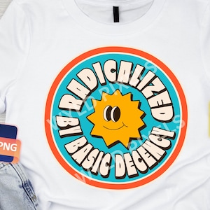 Könnte beinhalten: Weißes T-Shirt mit einem blauen, orangen und gelben Kreis-Motiv. Das Motiv zeigt eine lächelnde Sonne mit dem Text "I'm Radicalized by Basic Decency".