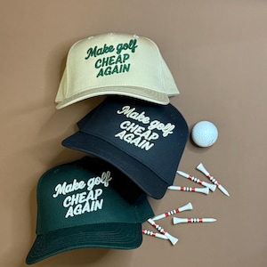 May include: Three baseball caps in cream, black, and dark green, each embroidered with "Make golf CHEAP AGAIN" in white or green. A golf ball and golf tees with red stripes are also present.
