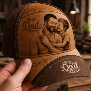 Może przedstawiać: Brązowa czapka bejsbolowa ze zdjęciem ojca i dziecka oraz napisem "Best Dad Ever". Czapka ma zakrzywiony daszek i przeszycia. Czapka jest wykonana z brązowego materiału.