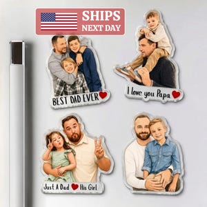 May include: A collection of clear acrylic magnets featuring illustrations of fathers with their children. Each magnet has a different design, with phrases like "Best Dad Ever," "I love you Papa," and "Just A Dad His Girl." The magnets are displayed on a metallic surface.
