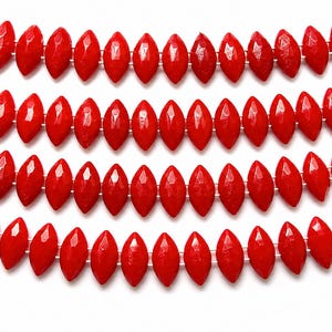May include: Four strands of bright red, faceted, marquise-shaped beads arranged in horizontal rows. Each bead features a pointed, elongated oval shape with multiple flat surfaces that reflect light, strung together on a thin, clear filament line.
