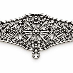 May include: A silver-toned metal jewelry connector featuring an intricate filigree pattern with a central sunburst design, symmetrical floral motifs on the sides, and three small circular loops for attachment at the top corners and bottom center.