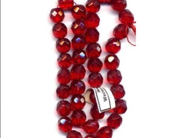 May include: A strand of faceted, translucent red beads arranged in a vertical loop. The beads are uniform in shape and size, reflecting light across their multiple surfaces. A small white rectangular tag with the text "Made in Western" is attached.