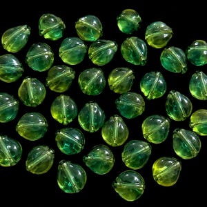 May include: A collection of translucent, round glass beads in varying shades of lime and emerald green. Each bead features a smooth, polished surface with a visible internal channel running through the center, creating a uniform appearance.