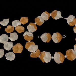 May include: A collection of frosted glass beads shaped like flower petals in translucent white and amber colors. The beads are arranged as a circular necklace with a small separate segment of two beads and a scattered pile of loose individual petal beads.