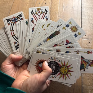 K&ouml;nnte beinhalten: Ein F&auml;cher aus Tarotkarten, die auf einer Holzoberfl&auml;che ausgebreitet sind. Die Karten zeigen farbenfrohe Illustrationen und den Text "Tarot" in einem schwarzen Kreis.