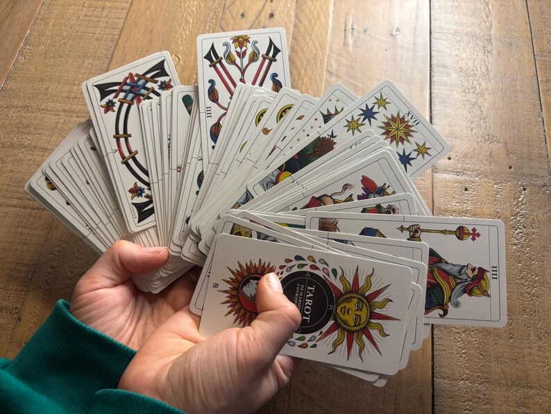 K&ouml;nnte beinhalten: Ein F&auml;cher aus Tarotkarten, die auf einer Holzoberfl&auml;che ausgebreitet sind. Die Karten zeigen farbenfrohe Illustrationen und den Text "Tarot" in einem schwarzen Kreis.