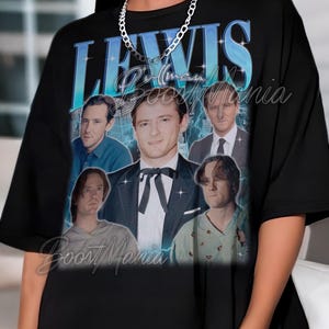Puede incluir: Camiseta negra con un diseño gráfico. El diseño presenta la palabra "LEWIS" en una fuente degradada azul, junto con varias imágenes de una persona. El texto "Pullman" y "Boost Mania" también son visibles en la camiseta.