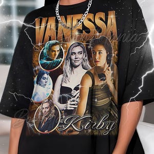 May include: Black t-shirt featuring a vintage-style design with the name "VANESSA" in gold lettering. The shirt includes multiple portraits of a woman, with the name "Kirby" below the portraits. A silver chain necklace is worn.