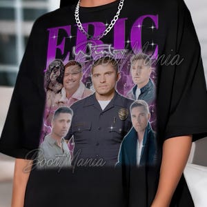 May include: Black t-shirt featuring a purple graphic with the name "ERIC" and several images of a man in a police uniform and other portraits. The text "Boost Mania" is also visible.