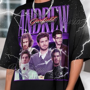 Pode incluir: Camiseta preta com um gráfico roxo com o nome "Andrew Garfield" e várias imagens do ator. O design tem uma estética vintage com detalhes de raios.