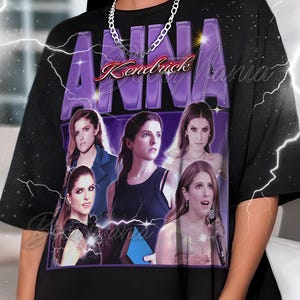 Könnte beinhalten: Schwarzes T-Shirt mit einer Collage von Bildern von Anna Kendrick, mit dem Namen "Anna Kendrick Mania" in lila und roter Schrift. Das Shirt hat einen Rundhalsausschnitt und kurze Ärmel.