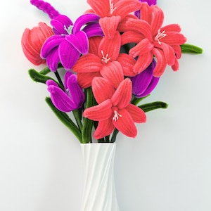 Può includere: Un bouquet di fiori fatti a mano in un vaso bianco. I fiori sono rossi, rosa e viola, con steli verdi. Il vaso ha un design a spirale.