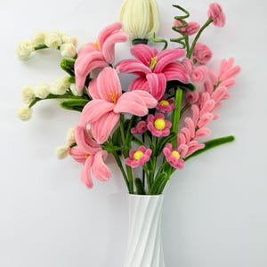 Può includere: Un bouquet di fiori rosa e bianchi in un vaso bianco. I fiori sono fatti di un materiale morbido e soffice e hanno steli verdi. Il vaso ha un design a spirale.
