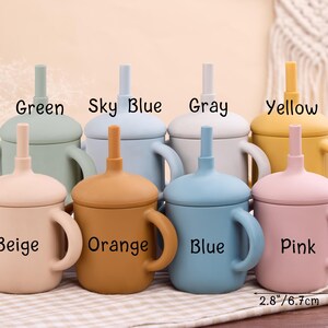 May include: A collection of colorful silicone baby cups with handles and straws. The cups are in various colors, including green, sky blue, gray, yellow, beige, orange, blue, and pink. Each cup is labeled with its color name. The cups measure 4.3 inches (10.9 cm) tall and 2.8 inches (6.7 cm) wide.