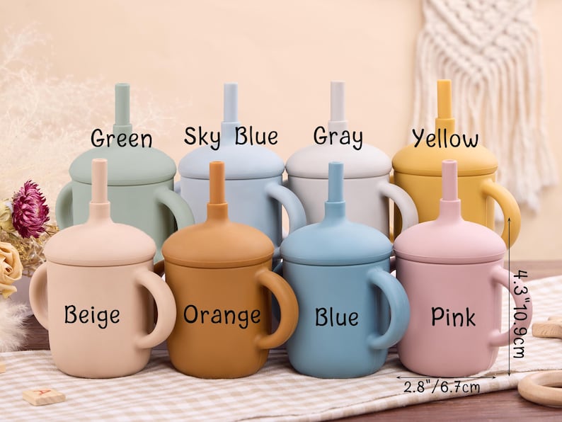 May include: A collection of colorful silicone baby cups with handles and straws. The cups are in various colors, including green, sky blue, gray, yellow, beige, orange, blue, and pink. Each cup is labeled with its color name. The cups measure 4.3 inches (10.9 cm) tall and 2.8 inches (6.7 cm) wide.