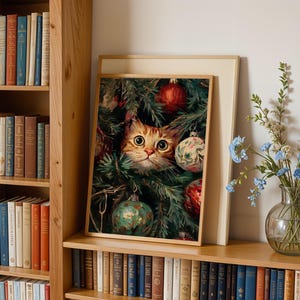 May include: A framed print featuring a ginger cat peeking through a Christmas tree decorated with ornaments. The print is displayed on a wooden shelf with a collection of books and a vase of flowers.