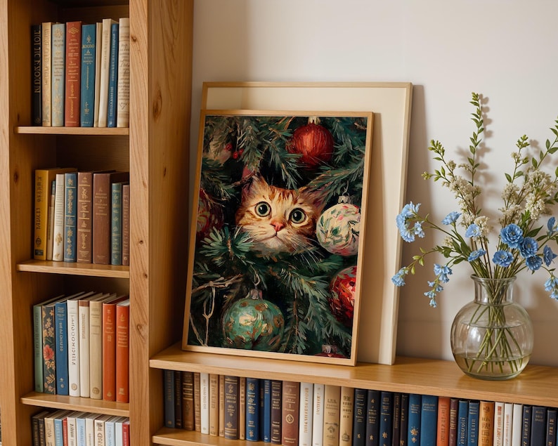 May include: A framed print featuring a ginger cat peeking through a Christmas tree decorated with ornaments. The print is displayed on a wooden shelf with a collection of books and a vase of flowers.