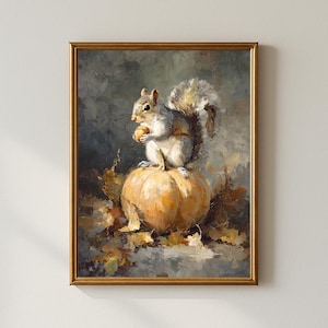 May include: A framed painting depicts a squirrel perched atop a pumpkin, holding a nut. The artwork features a warm color palette of orange, gray, and brown, with autumn leaves scattered around the pumpkin. The painting is enclosed in a gold frame.