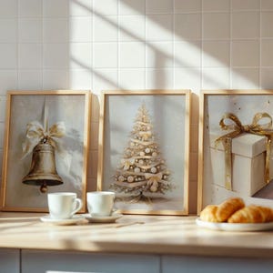 May include: Three framed Christmas-themed art prints. One features a bell with a bow, another a decorated tree, and the last a gift box with a bow. The prints are in light wooden frames, with a white background and gold accents.