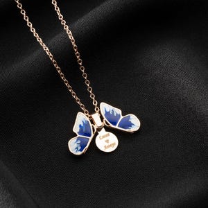 May include: A rose gold necklace with two blue and white butterfly charms and a small round charm with the text "Love Always".