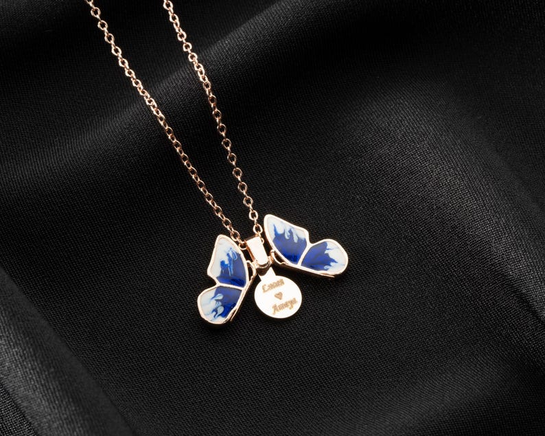 May include: A rose gold necklace with two blue and white butterfly charms and a small round charm with the text "Love Always".