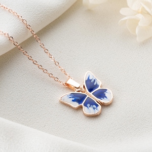 May include: A delicate rose gold chain necklace featuring a blue and white butterfly pendant. The butterfly has a marbled design and is a statement piece.