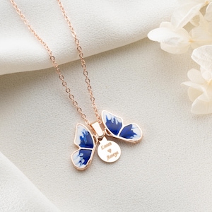 May include: A rose gold necklace featuring a blue and white butterfly pendant. The pendant has a small round charm inscribed with the words "Love Always".