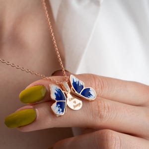 May include: A rose gold chain necklace with a blue and white butterfly pendant. The butterfly has a small disc charm with the words "Love is Magic" engraved on it.