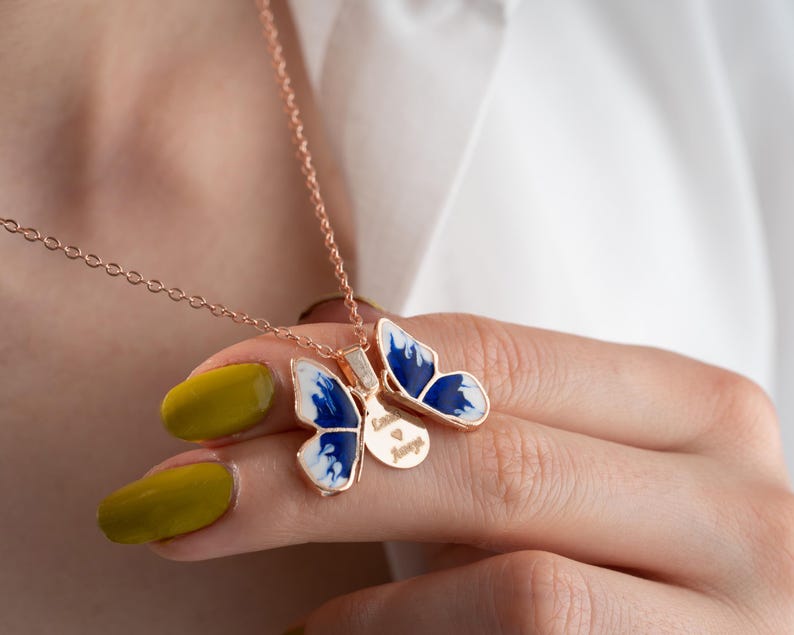 May include: A rose gold chain necklace with a blue and white butterfly pendant. The butterfly has a small disc charm with the words "Love is Magic" engraved on it.