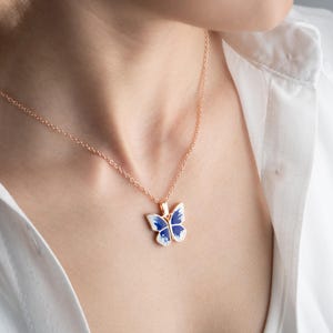 May include: A rose gold chain necklace with a blue and white enamel butterfly pendant.