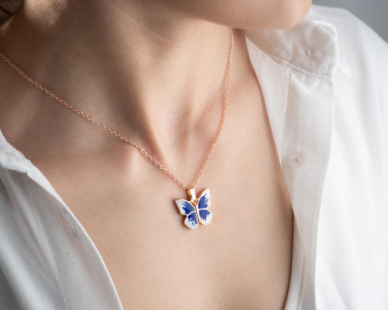 May include: A rose gold chain necklace with a blue and white enamel butterfly pendant.