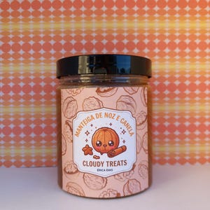 May include: A jar with a black lid and a label featuring a cartoon pumpkin, star, and cinnamon stick. The label reads "MANTEIGA DE NOZ E CANELA" and "CLOUDY TREATS ERICA DIAS" on a pink background with a walnut pattern.