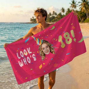 Pode incluir: Uma toalha de praia magenta com o texto "LOOK WHO'S 18!" e uma foto de uma jovem com um chapéu de festa. A toalha é decorada com confetes e é segurada por uma pessoa na praia.